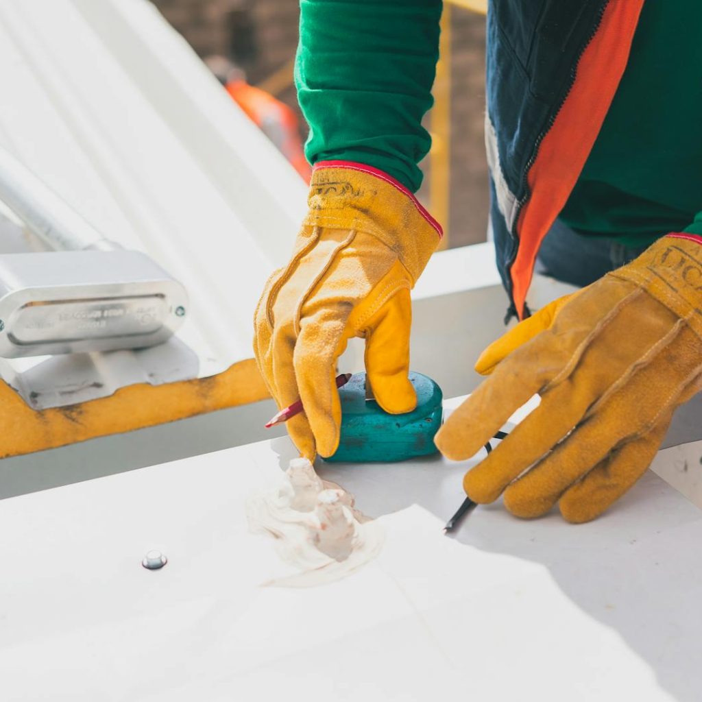 Electrician measuring on rooftop, wearing protective gloves, during daylight.